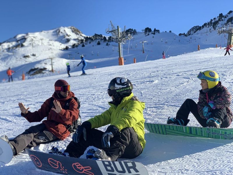 Grupo de alumnos sentados en la nieve durante una clase de snowboard en Baqueira Beret