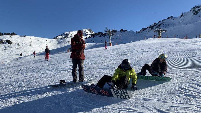 Clase de snowboard en las pistas de Baqueira Beret con los remontes al fondo