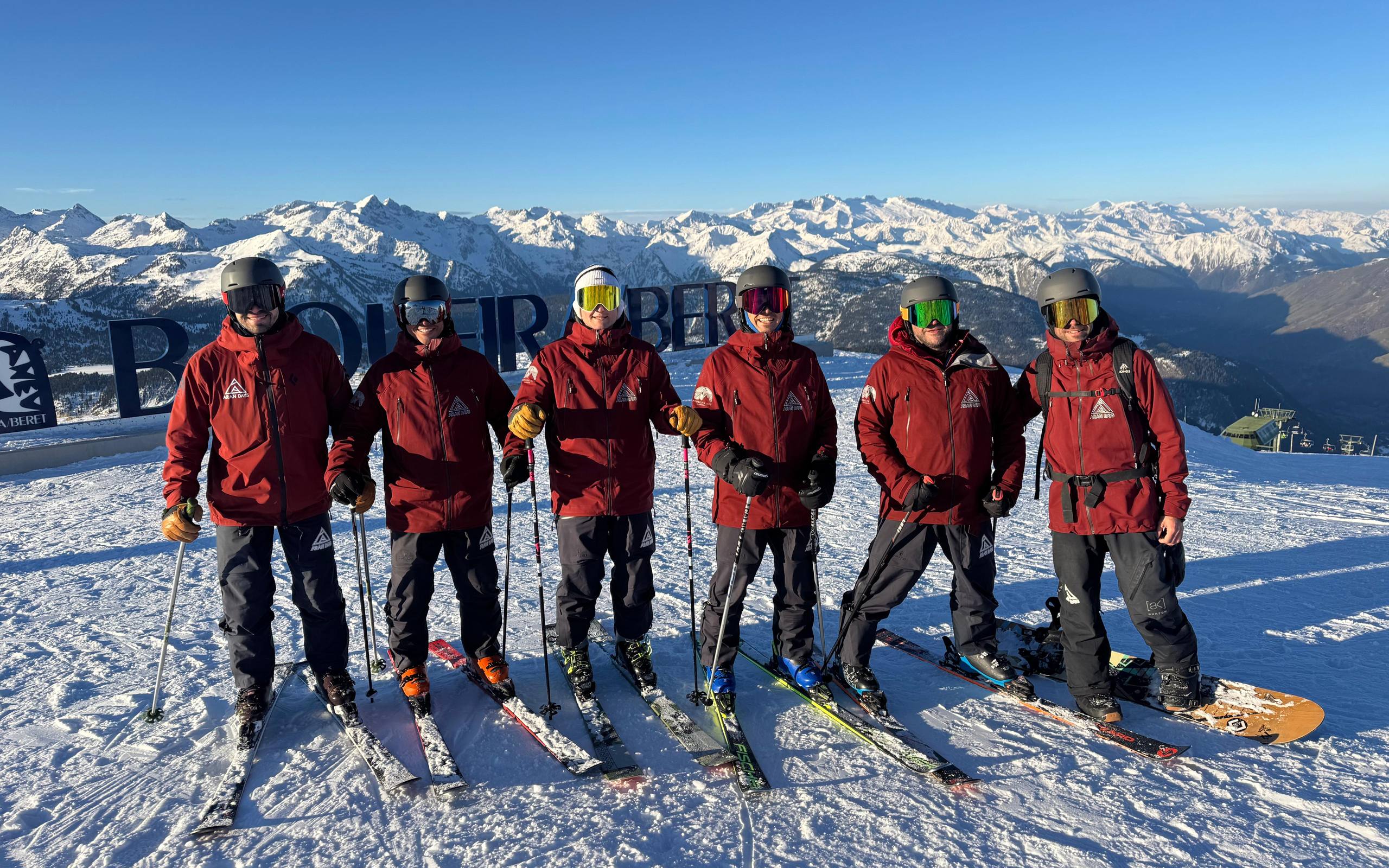 Equipo de instructores de Aran Days posando con esquís y snowboard en lo alto de Baqueira Beret